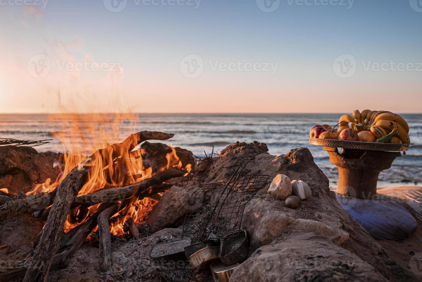 Fresh fruits in plate beside bonfire with burning firewood on beach in evening photo