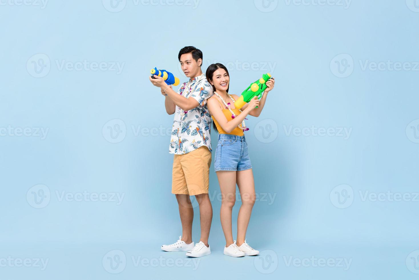 Young Asian couple in summer outfits with water guns in studio blue background for Songkran festival in Thailand and southeast Asia photo