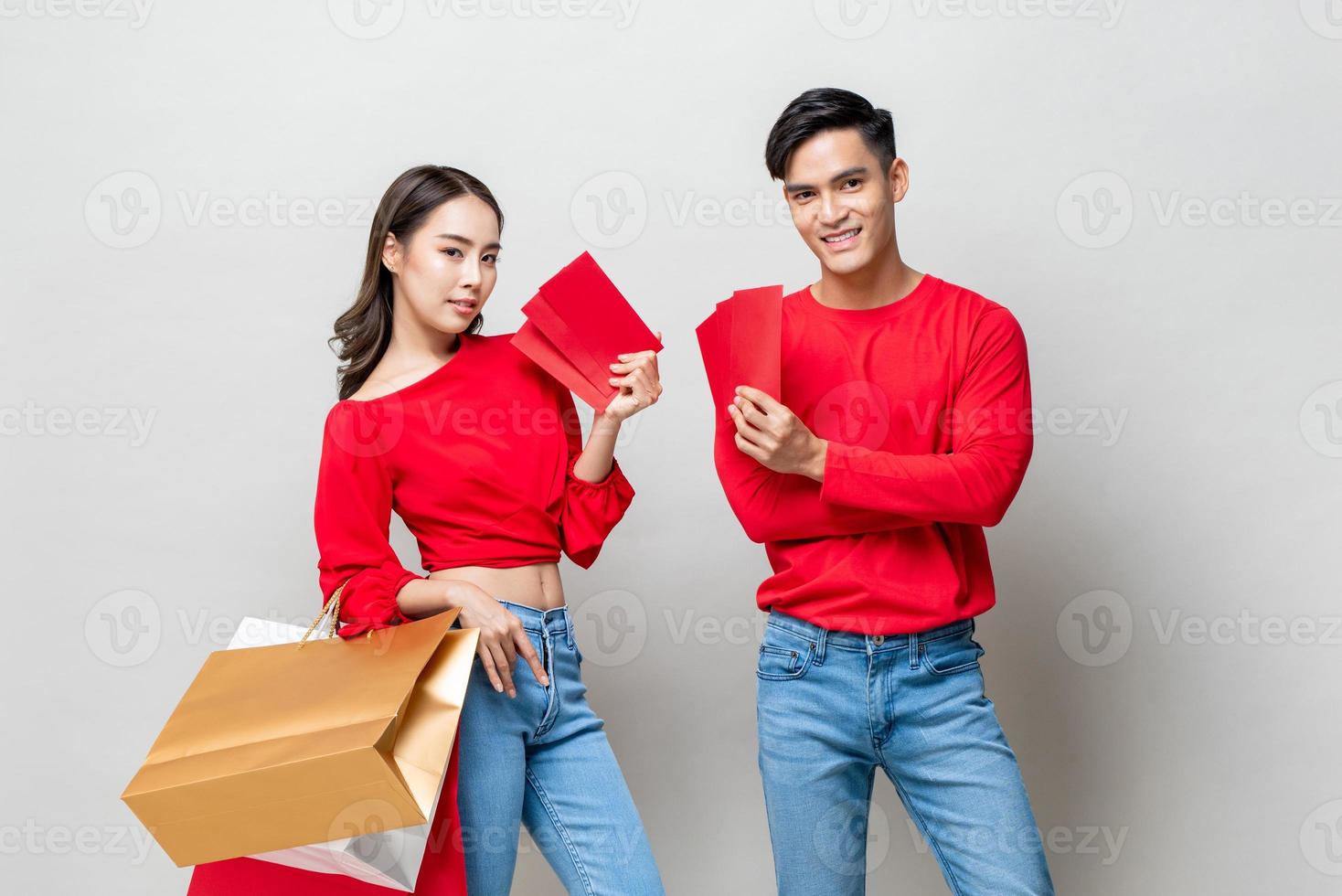 feliz amante de la pareja asiática con bolsas de compras y sobres rojos aislados en un estudio gris claro para el concepto de venta de año nuevo chino foto