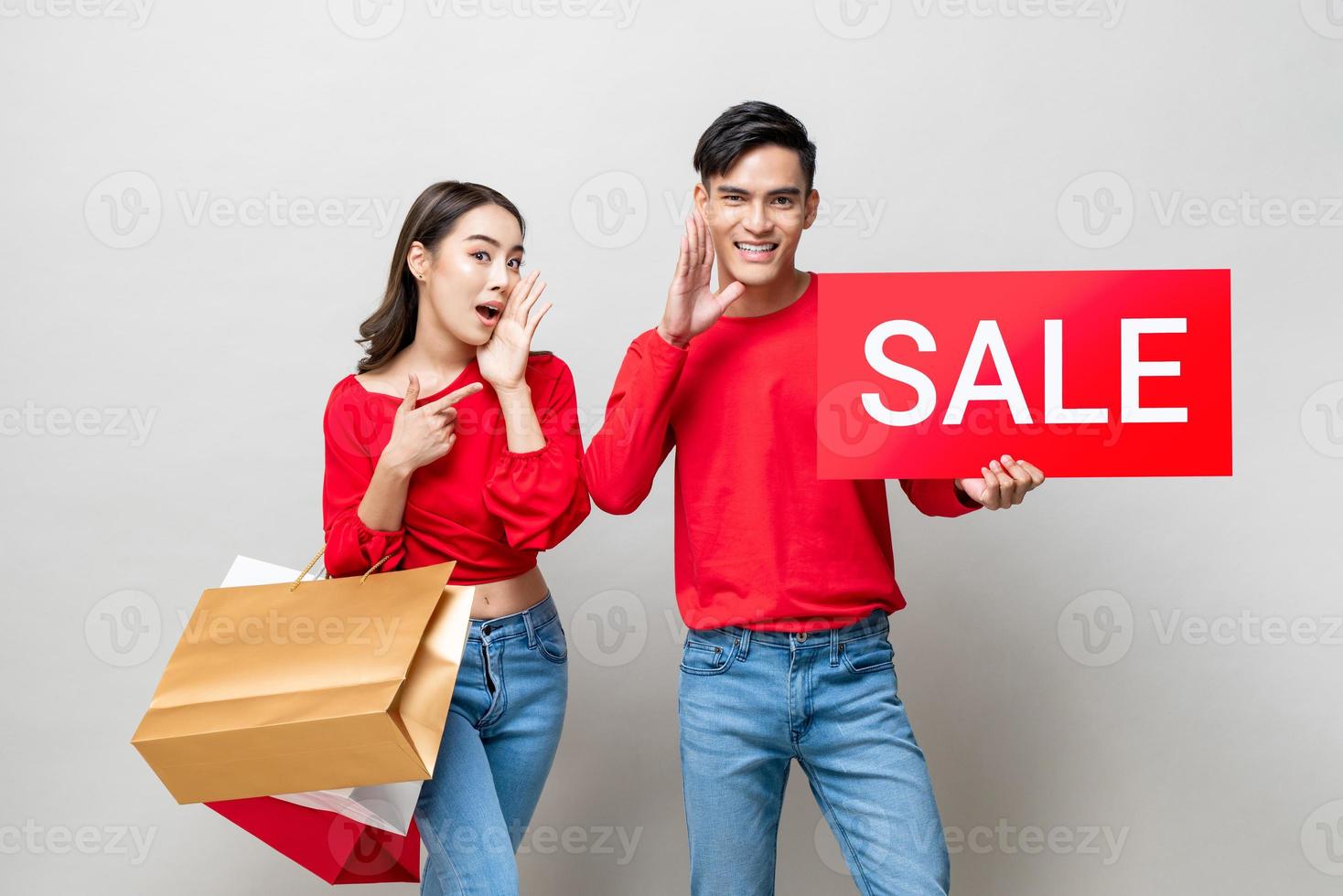 Asian couple with bags and red sale sign in isolated gray studio background for Chinese new year shopping concept photo