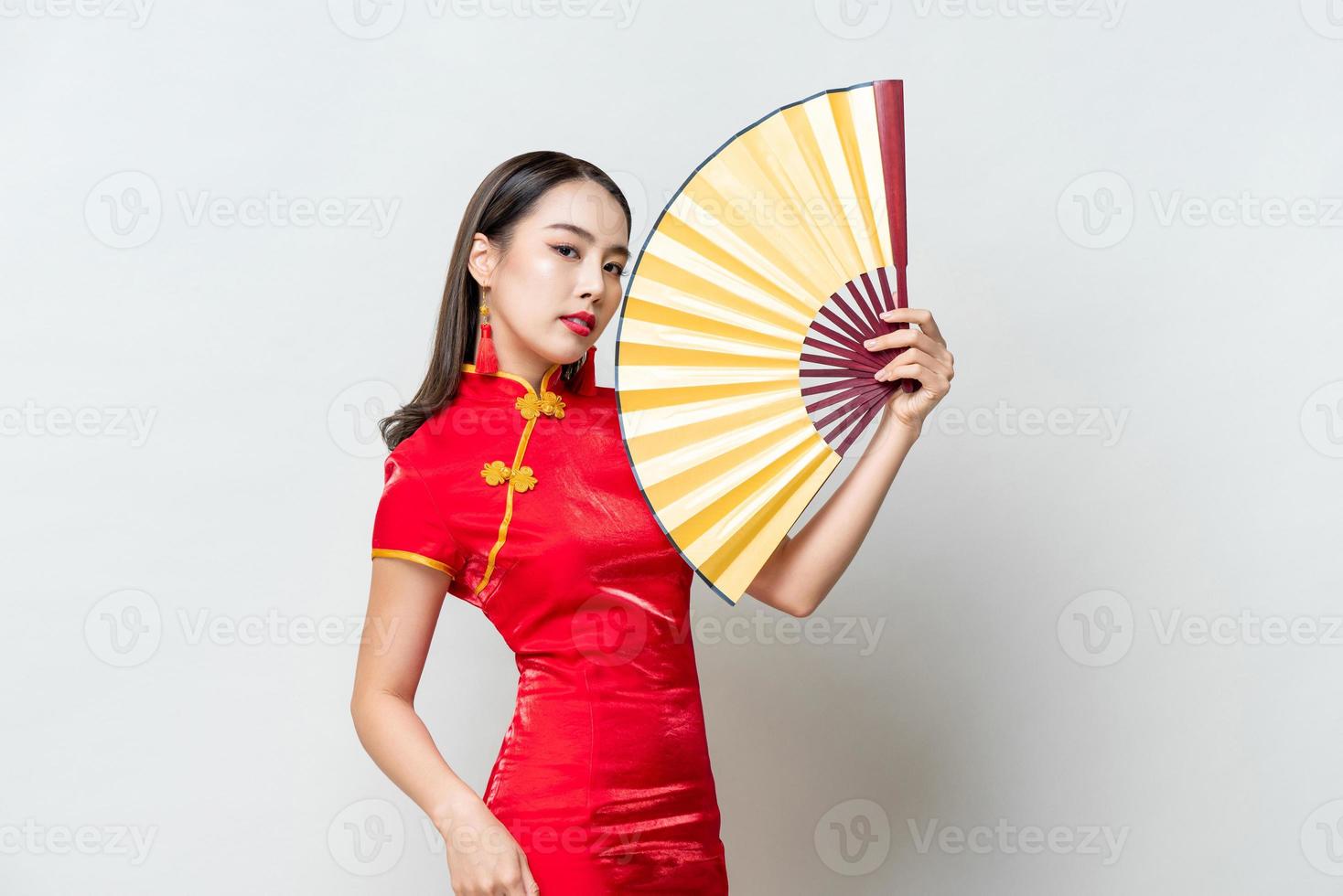 Beautiful Asian woman wearing traditional cheongsam qipao dress holding golden fan in isolated studio light gray background for chinese new year concept photo