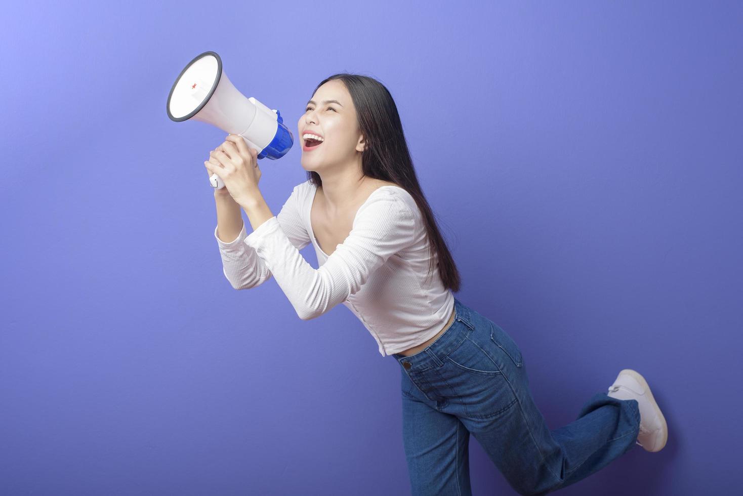 retrato de una joven hermosa mujer sonriente está usando un megáfono para anunciar sobre un estudio aislado de fondo morado foto