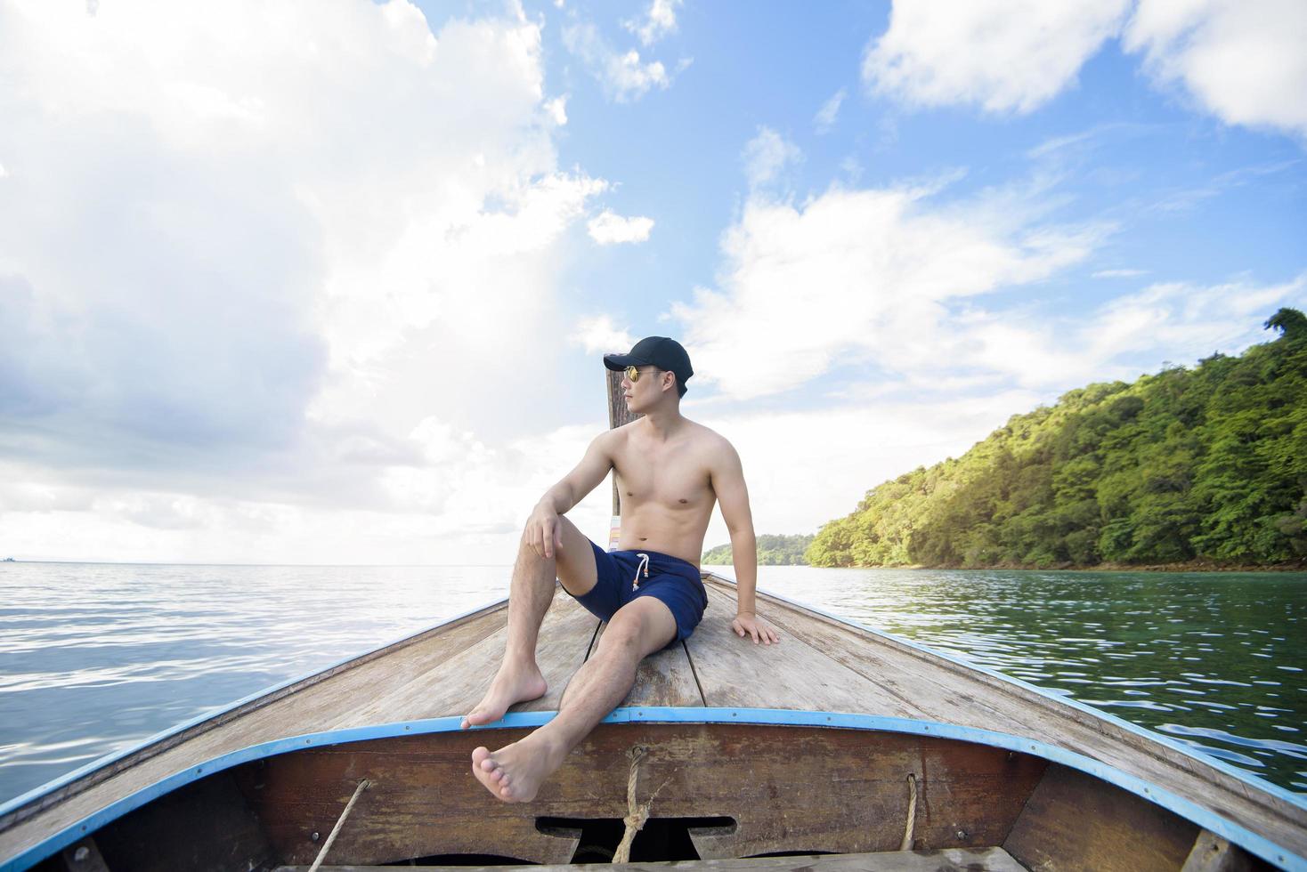 vista del hombre en traje de baño disfrutando en el tradicional bote de cola larga tailandés sobre la hermosa montaña y el océano, islas phi phi, tailandia foto