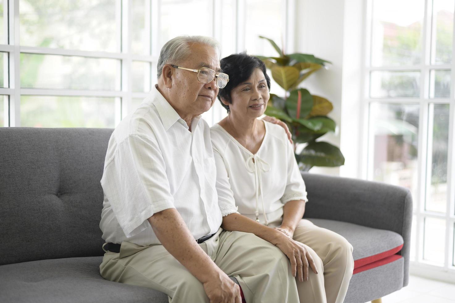 Elderly Asian couple watching television sitting on a sofa photo