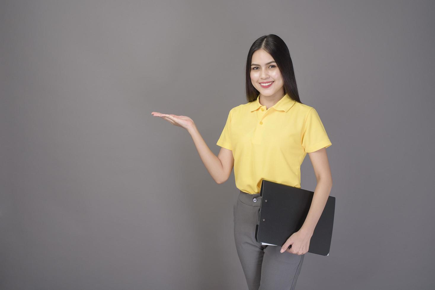 young confident beautiful woman wearing yellow shirt is holding documents on grey background studio photo