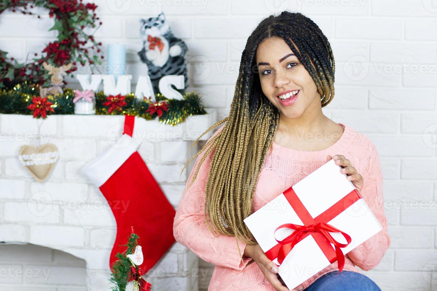 niña feliz sosteniendo regalos cerca de la chimenea y las fiestas navideñas diciendoation foto