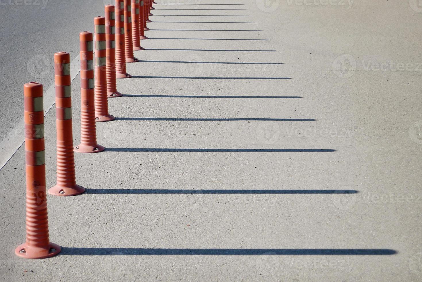 Red regilation poles throwing shadows on the road. photo
