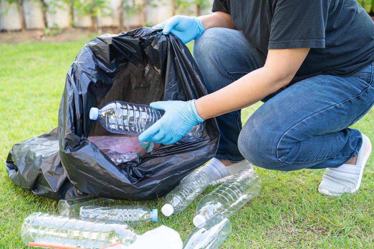 Asian woman volunteer carry water plastic bottles into garbage bag trash in park, recycle waste environment ecology concept. photo