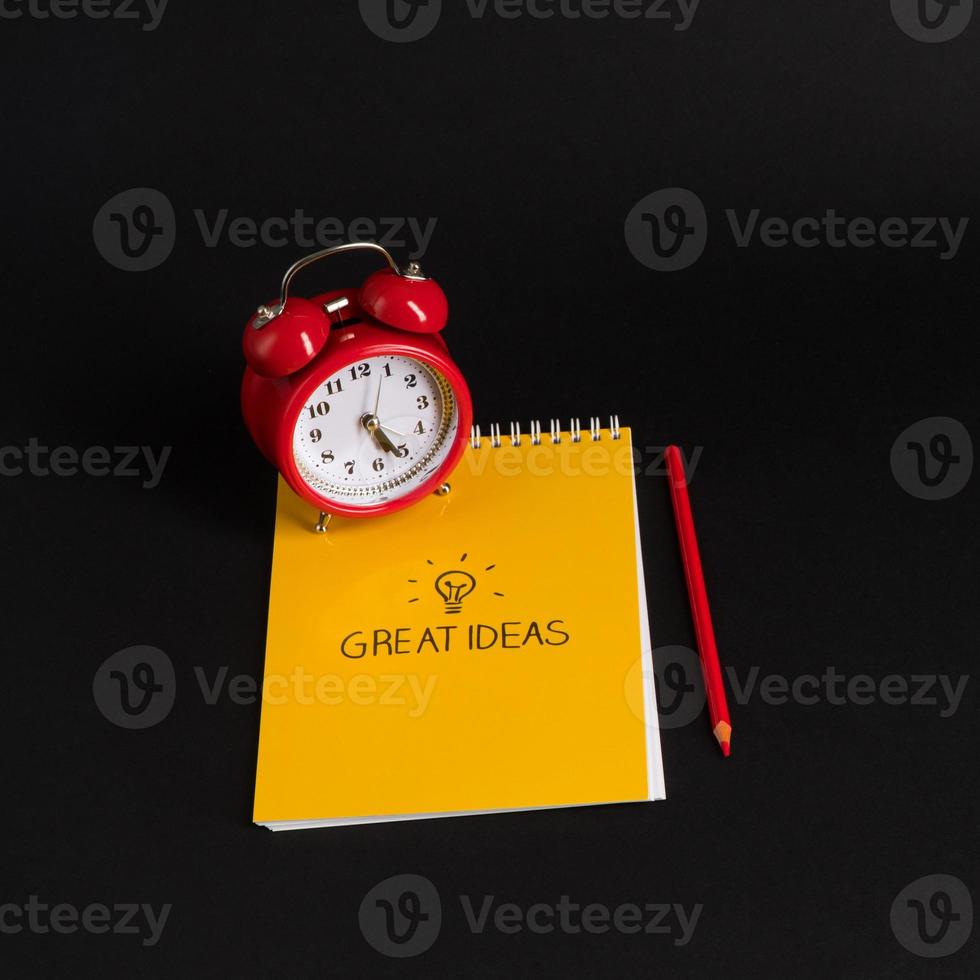 alarm clock with notepad and colored pencils on black background, isolated. back to school. great ideas photo