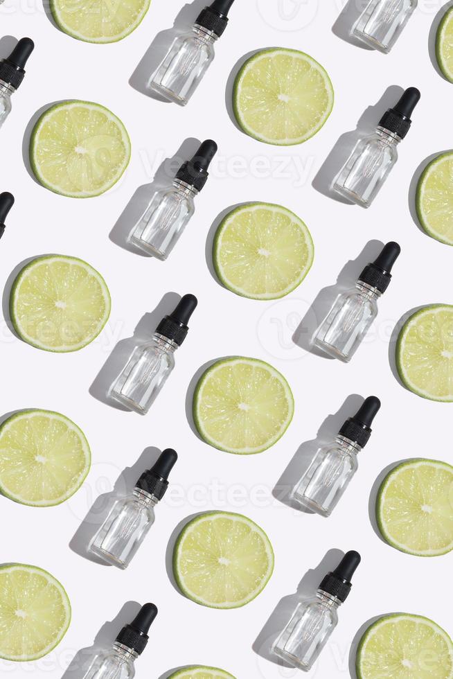 Top view dropper bottle of vitamin C serum, cosmetic oil and slices lime on white background. Creative cosmetics pattern vertical format photo