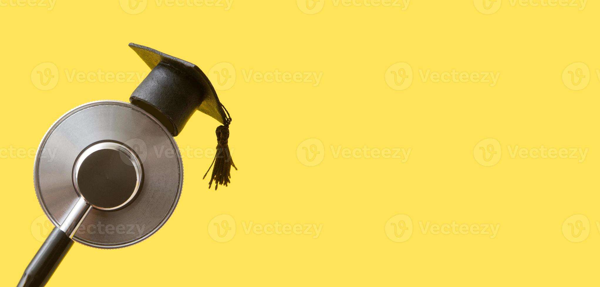 Graduation hat on medical stethoscope, yellow background with copy space banner format. Medical school, health care education or doctor's university degree concept photo