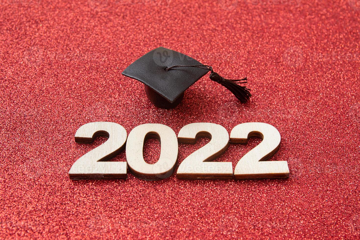 Graduat hat with wooden number 2022 on red glittering background. Education, leaning, class 2022 concept photo