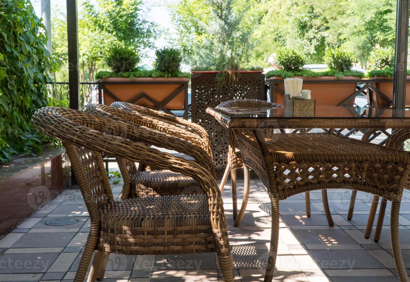 tables and wicker chairs in outdoor summer cafe with flower beds photo