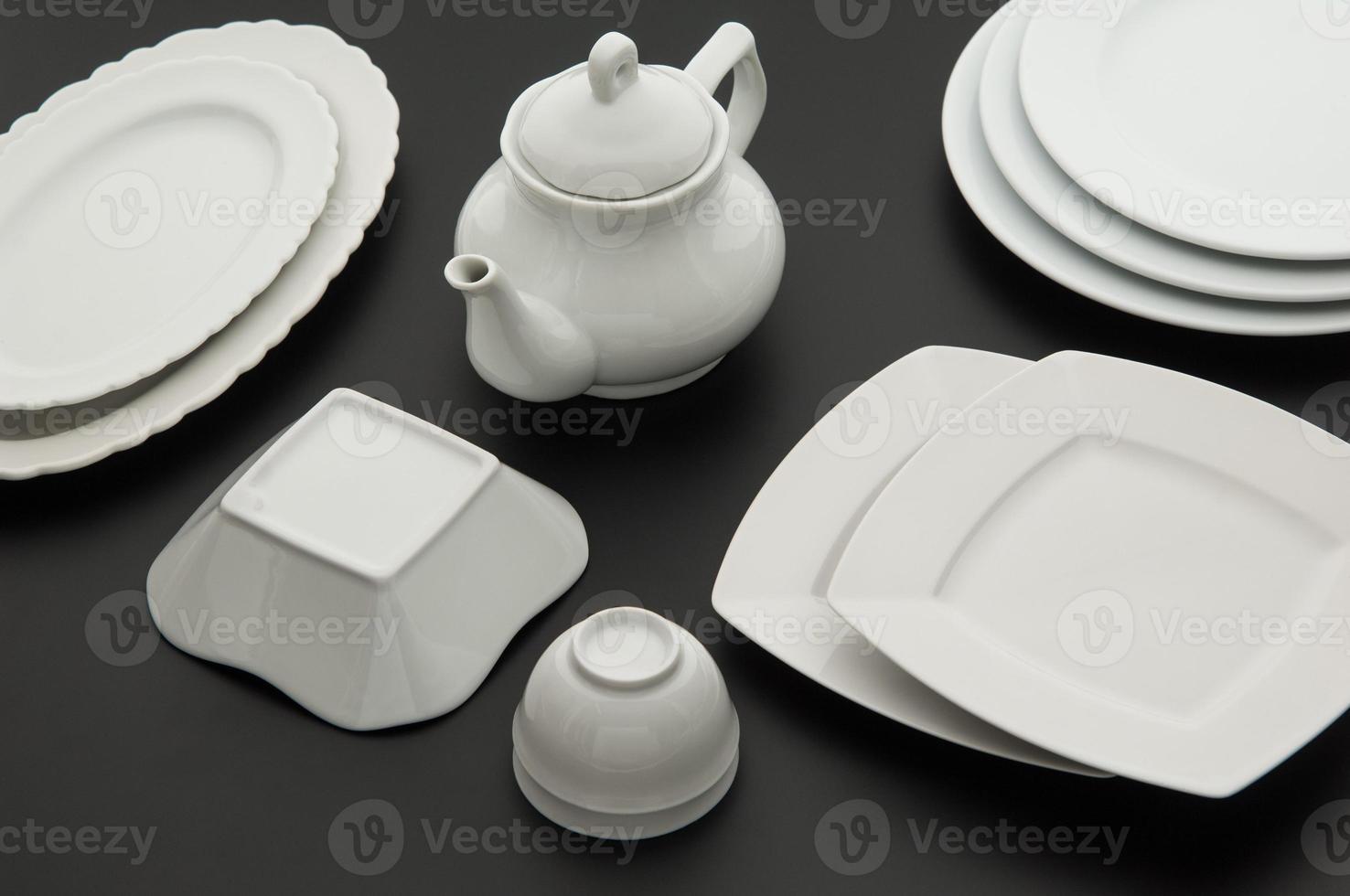set of kitchen white ceramic tableware on black background, top view photo