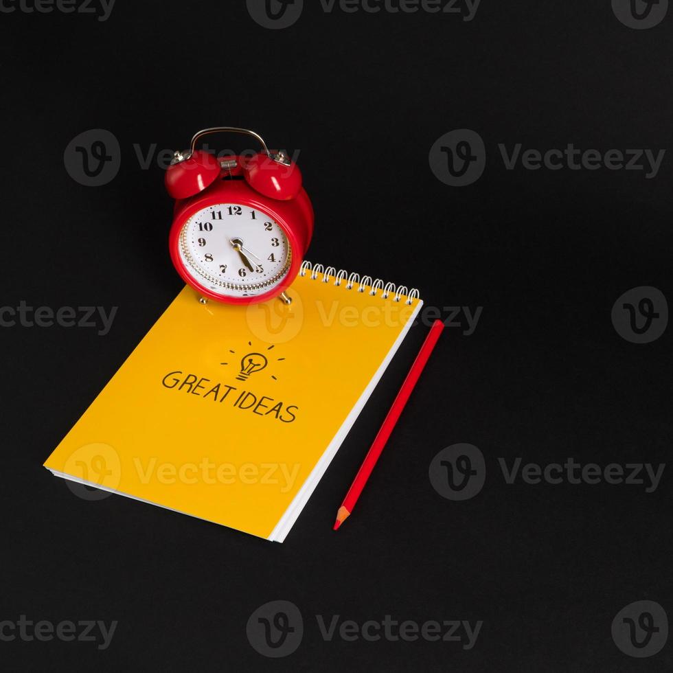 alarm clock with notepad and colored pencils on black background, isolated. back to school. great ideas photo
