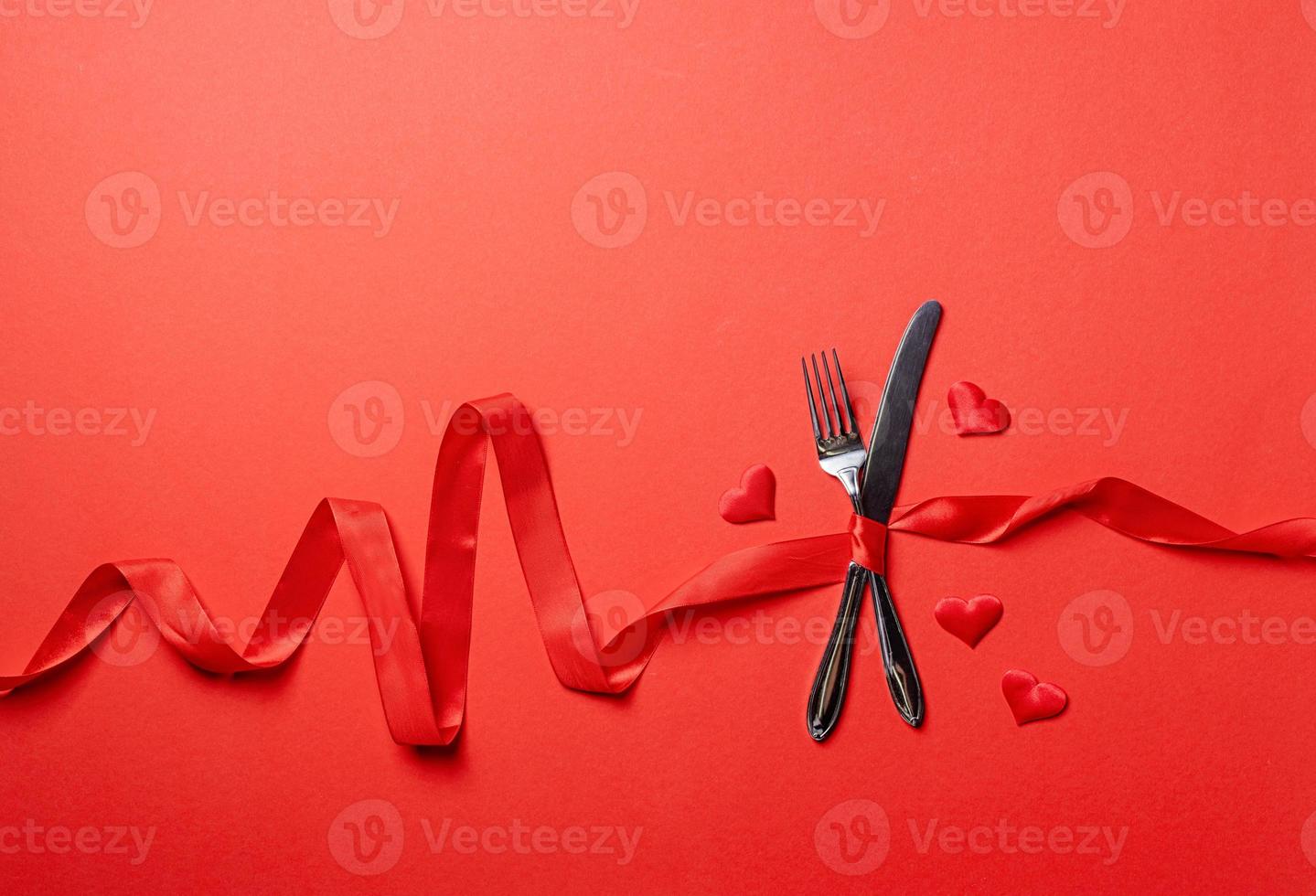 Fork and knife tied with a red ribbon in a shape of heart rate on red background photo