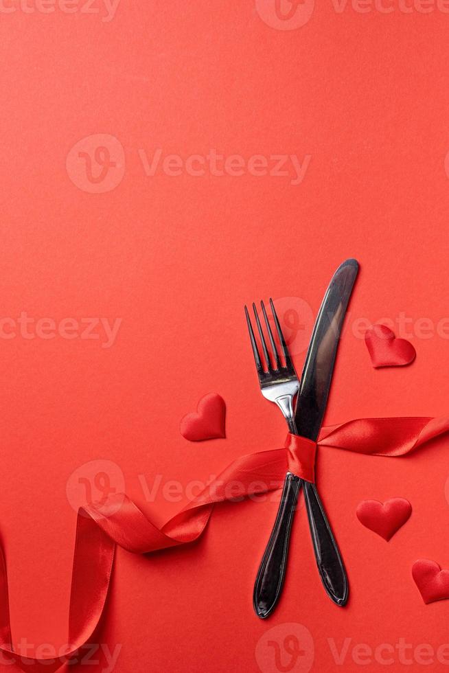 tenedor y cuchillo atados con una cinta roja en forma de frecuencia cardíaca sobre fondo rojo foto
