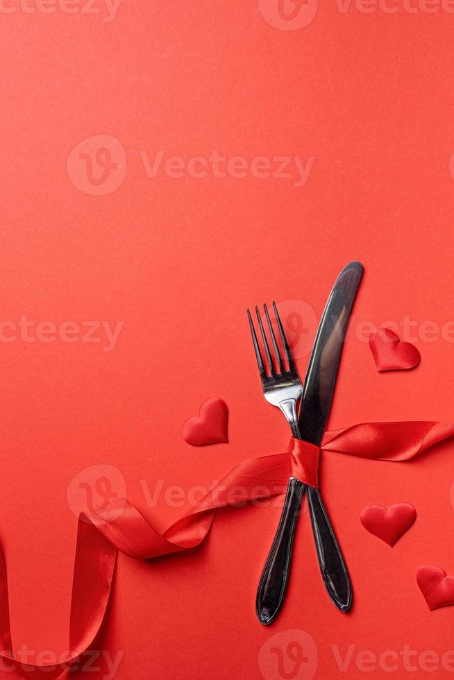 Fork and knife tied with a red ribbon in a shape of heart rate on red background photo