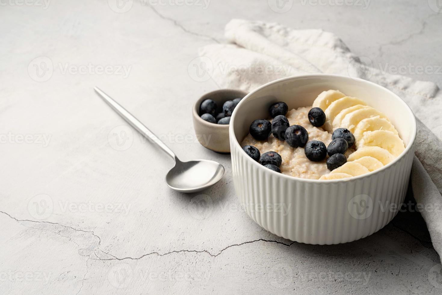 avena. avena con plátanos y arándanos para un desayuno o almuerzo saludable en una servilleta de lino y fondo de hormigón foto