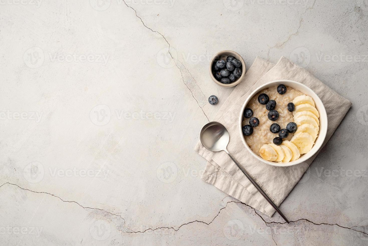 Oatmeal. Porridge with bananas and blueberries for healthy breakfast or lunch. Flat lay on linen napkin and concrete background photo