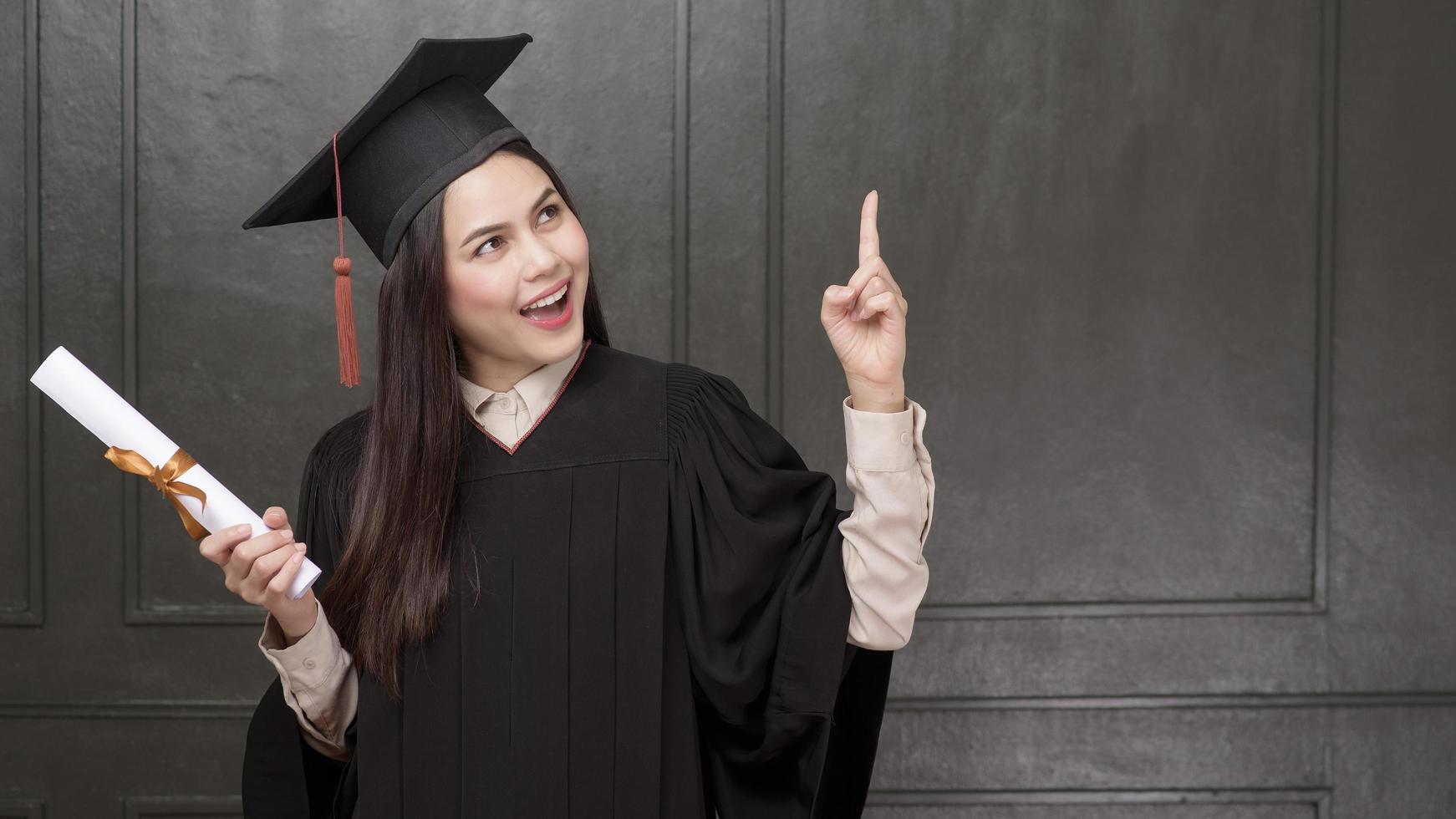 Portrait of young woman in graduation gown smiling and cheering on black background photo