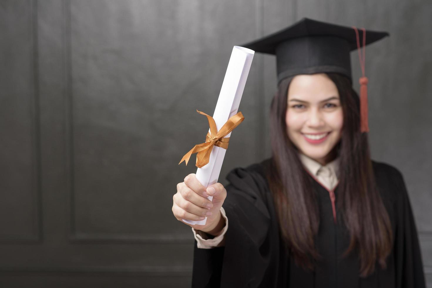 Portrait of young woman in graduation gown smiling and cheering on black background photo