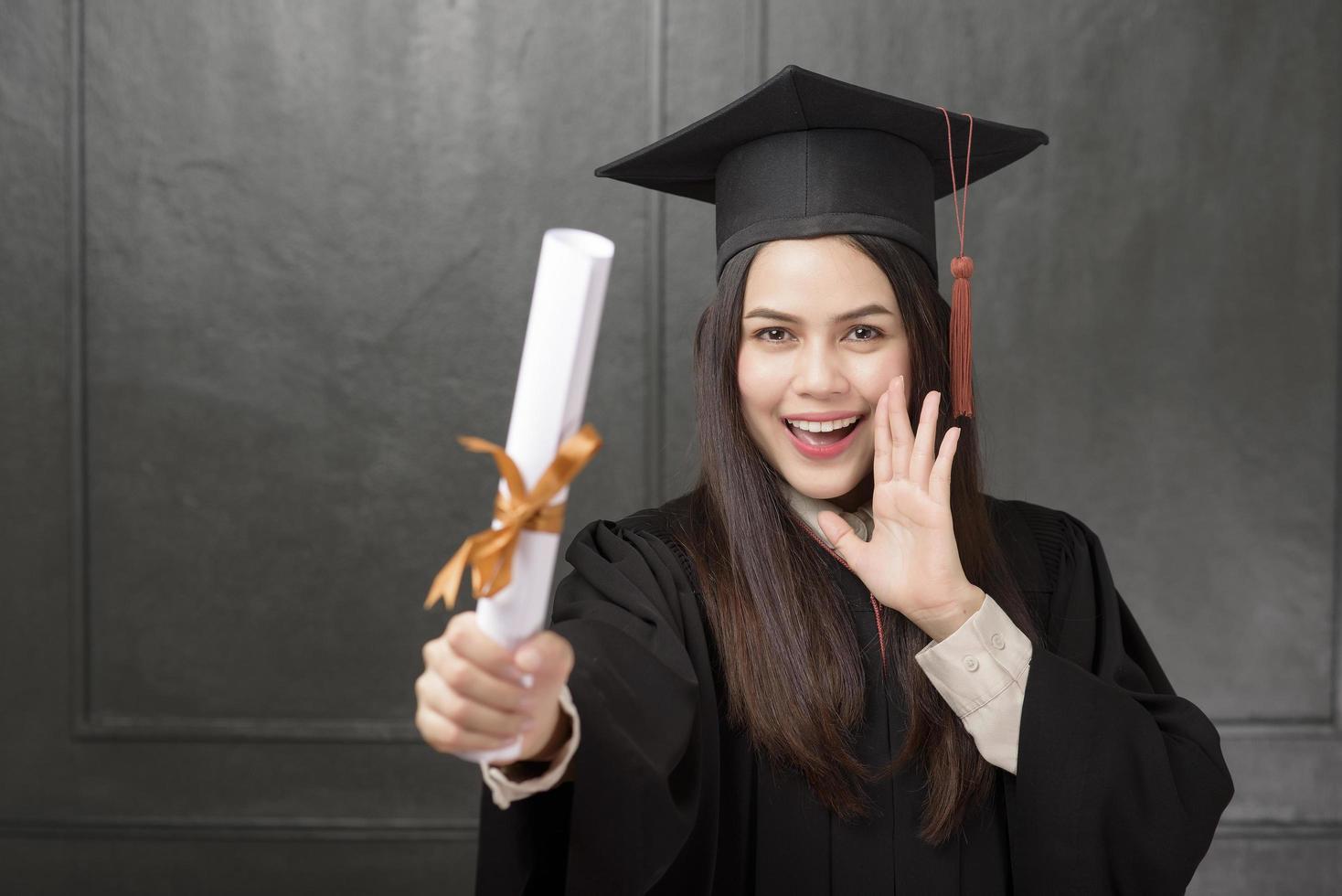 Portrait of young woman in graduation gown smiling and cheering on black background photo