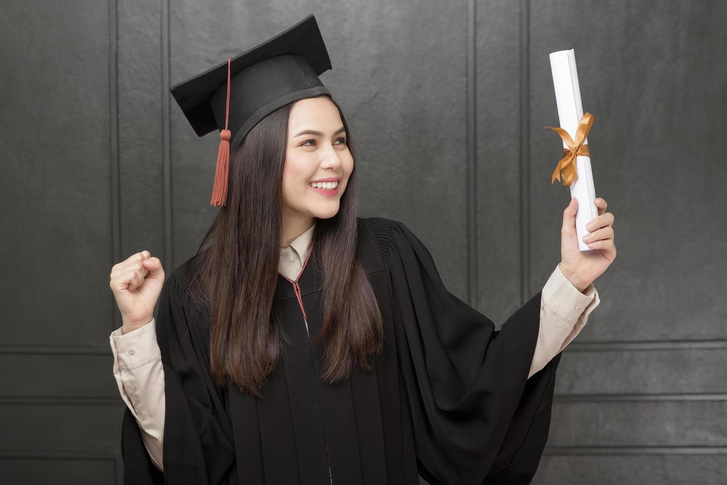 Portrait of young woman in graduation gown smiling and cheering on black background photo