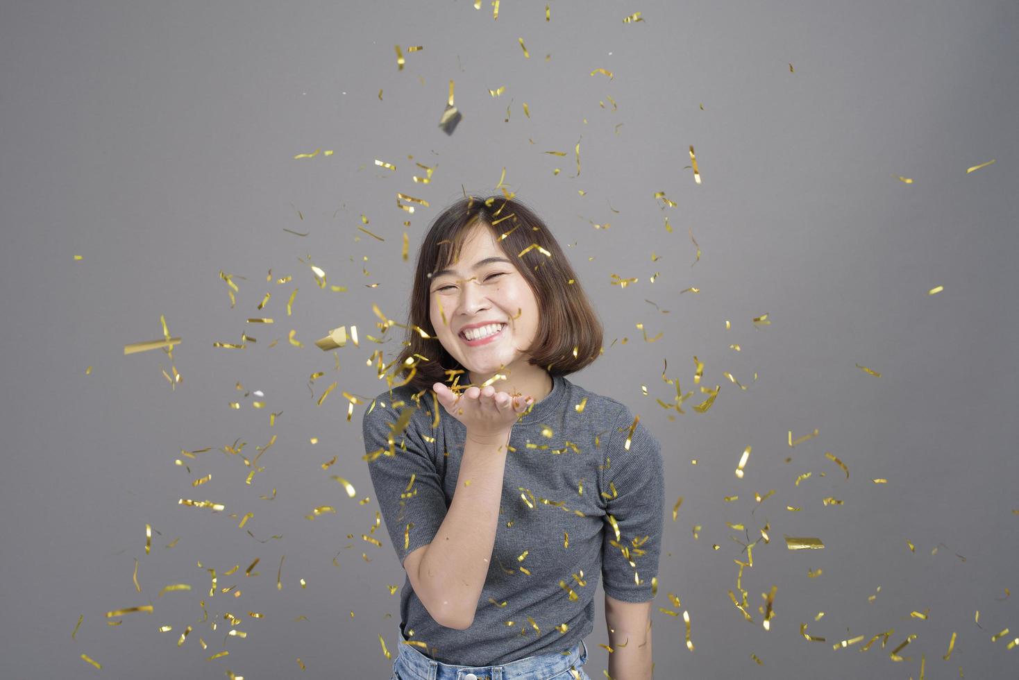 retrato de joven hermosa mujer asiática celebrando y jugando papel disparar estudio de fondo gris aislado, concepto de navidad y año nuevo. foto