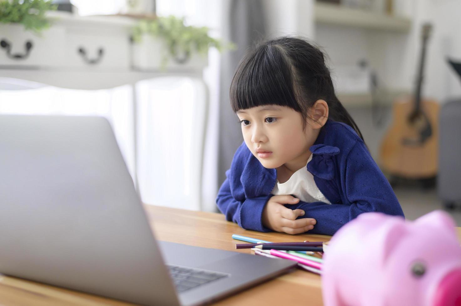 una niña linda está usando una computadora portátil para estudiar en línea a través de Internet en casa. concepto de aprendizaje electrónico durante el tiempo de cuarentena. foto