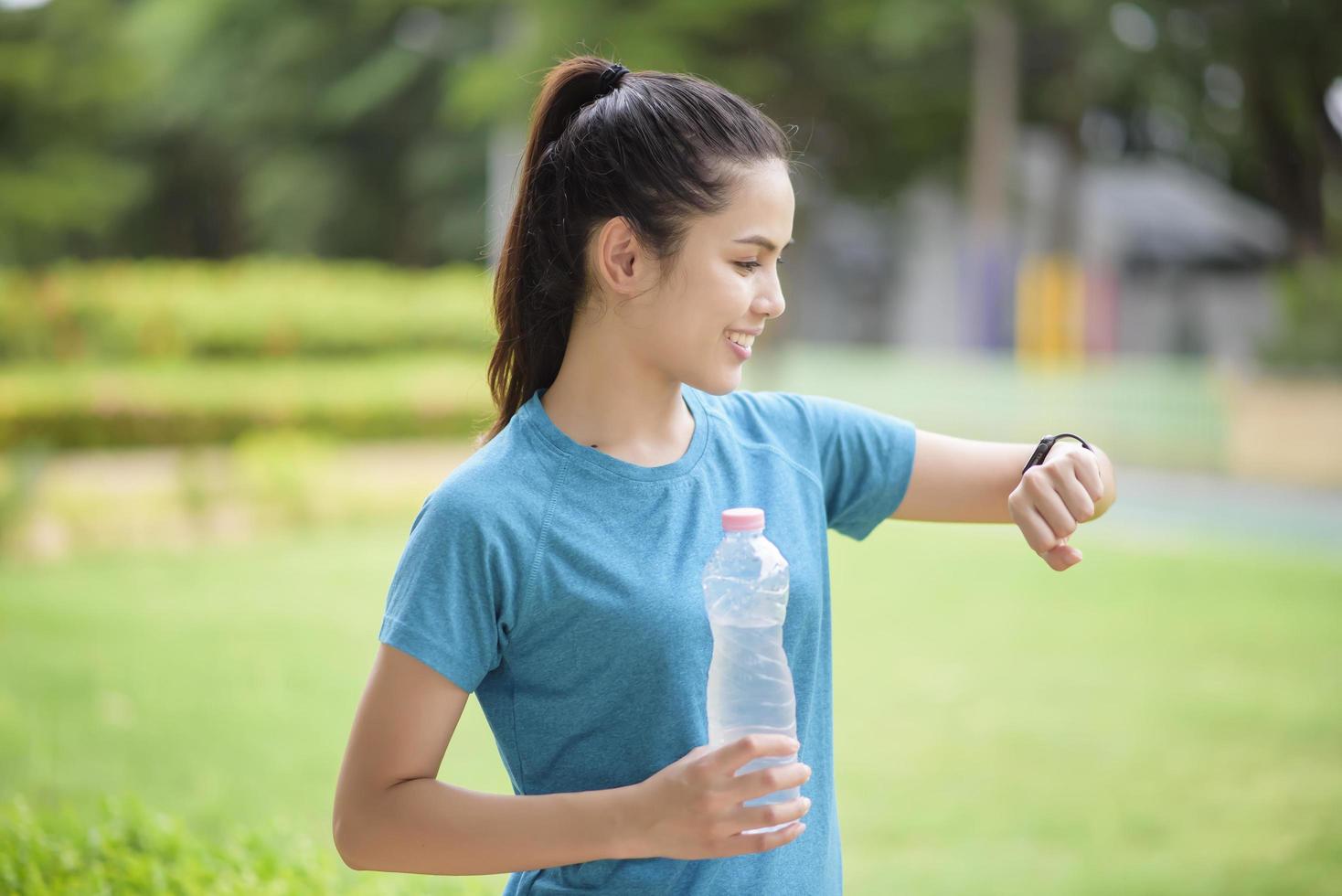 Happy young woman in sportswear using smart watch while exercising in park photo