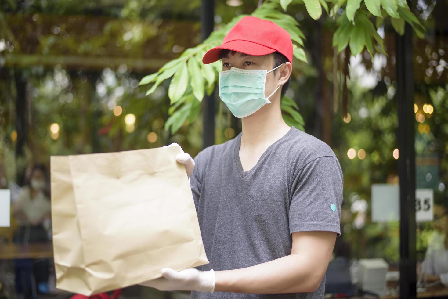 un repartidor asiático lleva mascarilla, sostiene una bolsa de comestibles, concepto de entrega a domicilio de seguridad foto