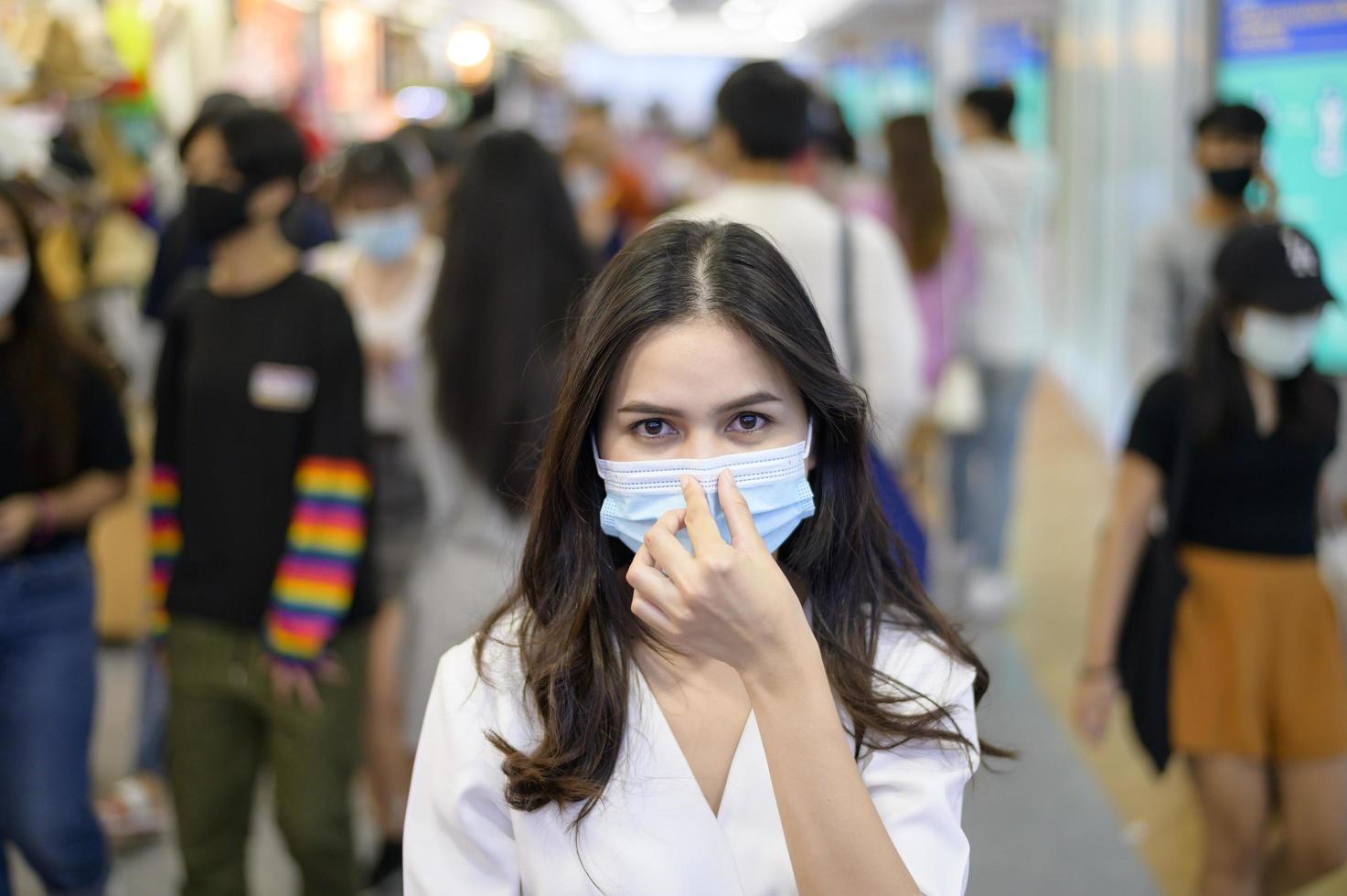 una mujer lleva una máscara protectora en la calle con gente abarrotada mientras la pandemia de covid-19, la protección contra el coronavirus, el concepto de estilos de vida seguros foto