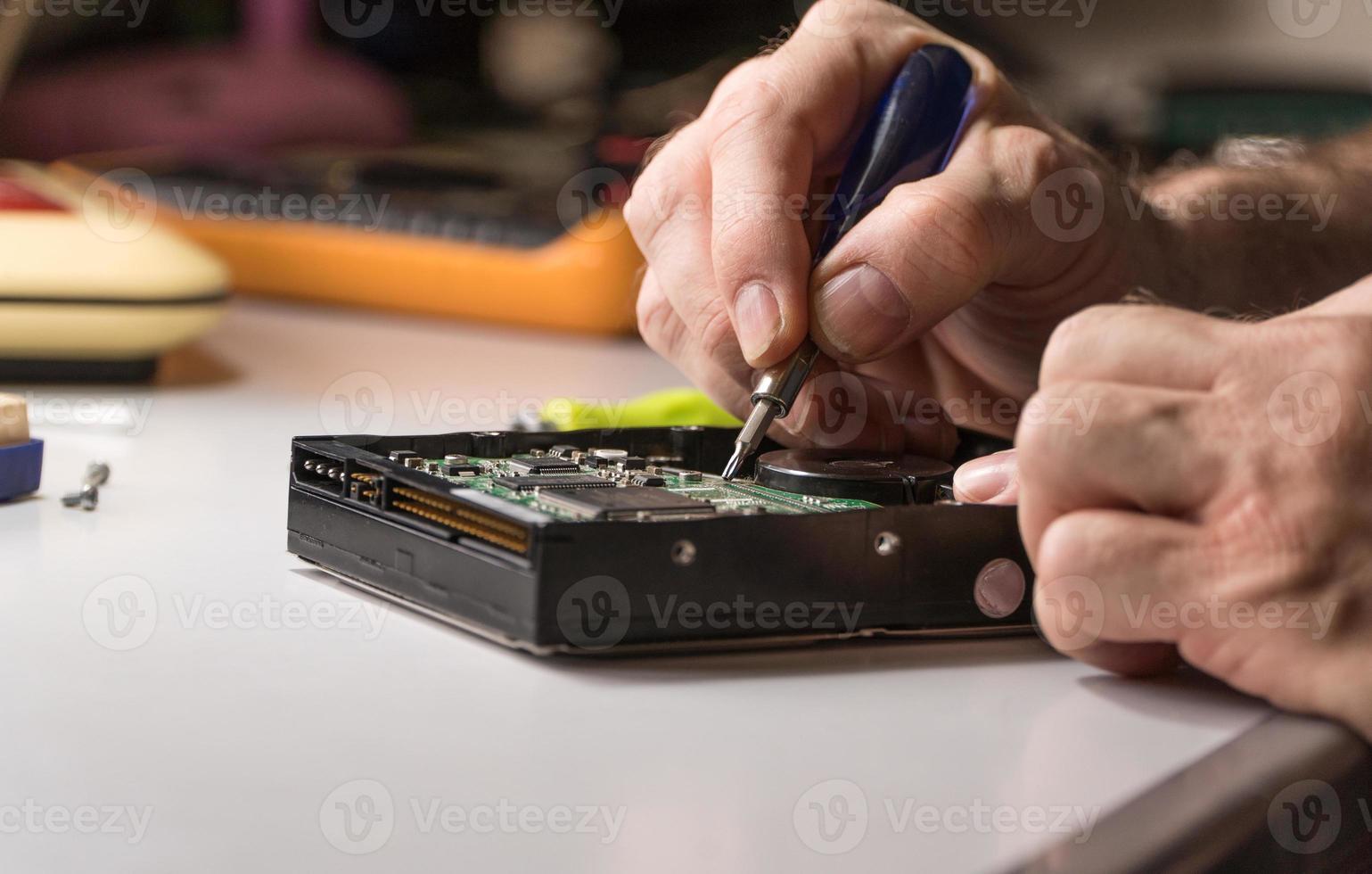 ingeniero electrónico repara el disco duro de la computadora. el tecnólogo con un destornillador desmonta el disco duro foto