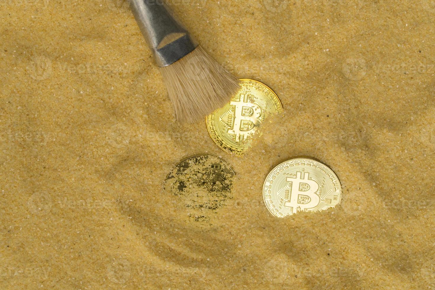 archaeologist with a brush clears the bitcoin coin on the golden sand. top view. finding and mining cryptocurrency photo