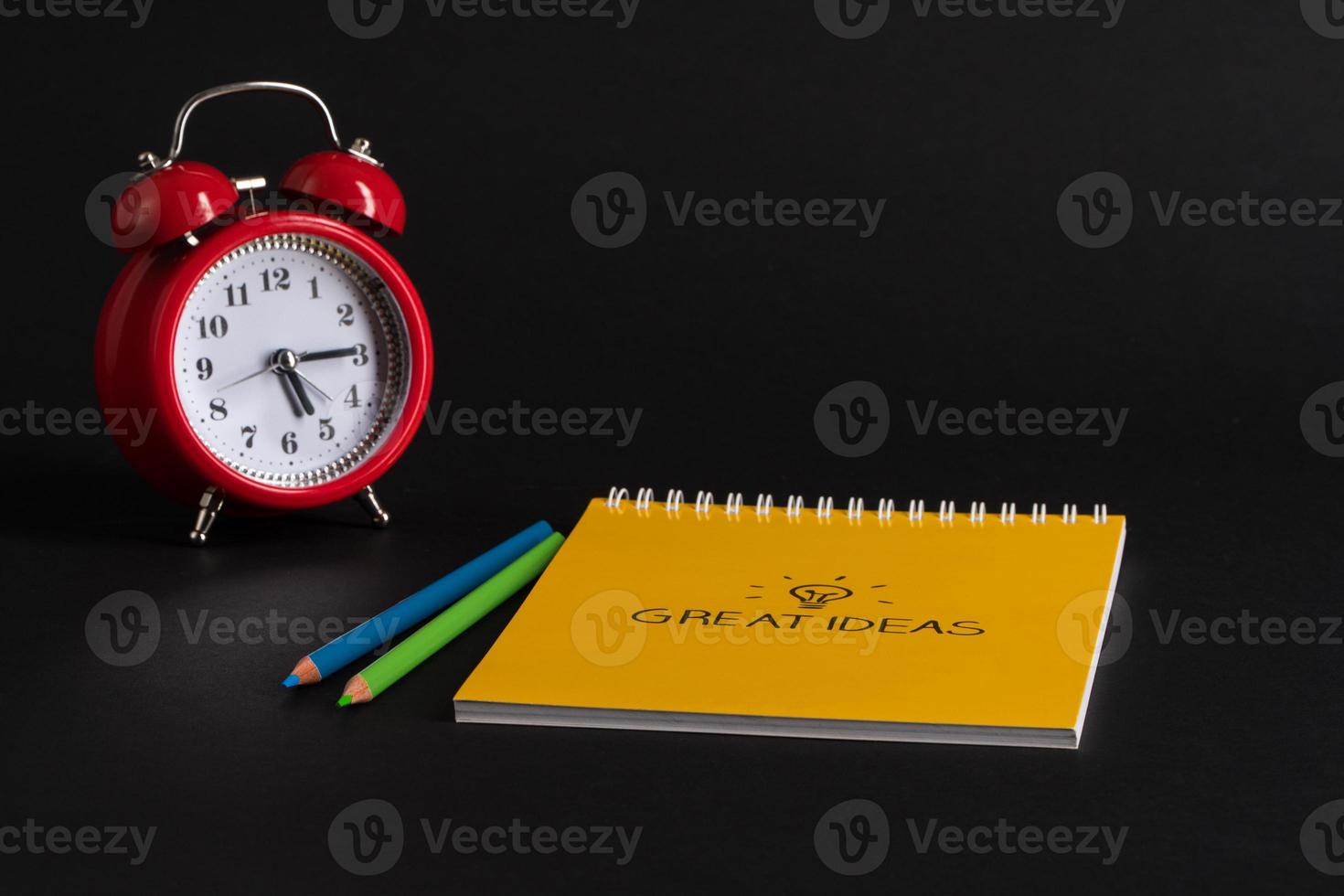 alarm clock with notepad and colored pencils on black background, isolated. back to school. great ideas photo