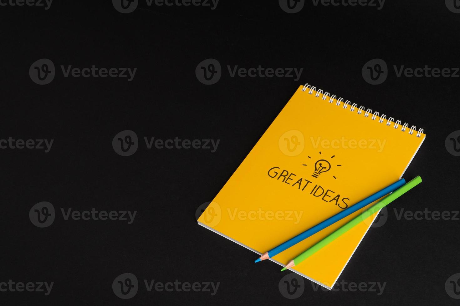 yellow notepad with colored pencils on black background, isolated. back to school. great ideas photo
