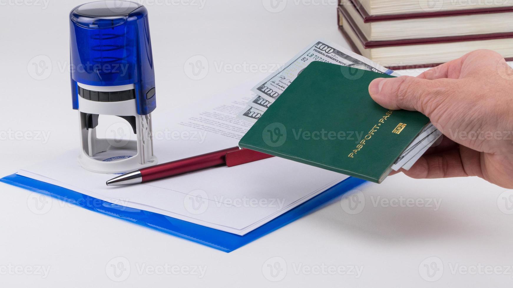 Hand holds out the green passport with US dollars on the background of documents and rubber stamp. Concept briber and corruption photo