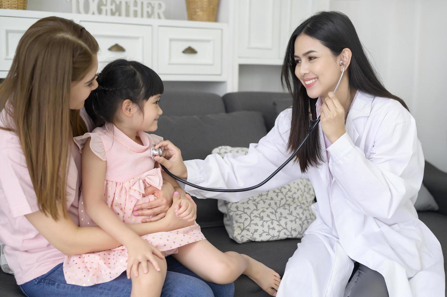 una doctora que sostiene un estetoscopio está examinando a una niña feliz en el hospital con su madre, concepto médico foto