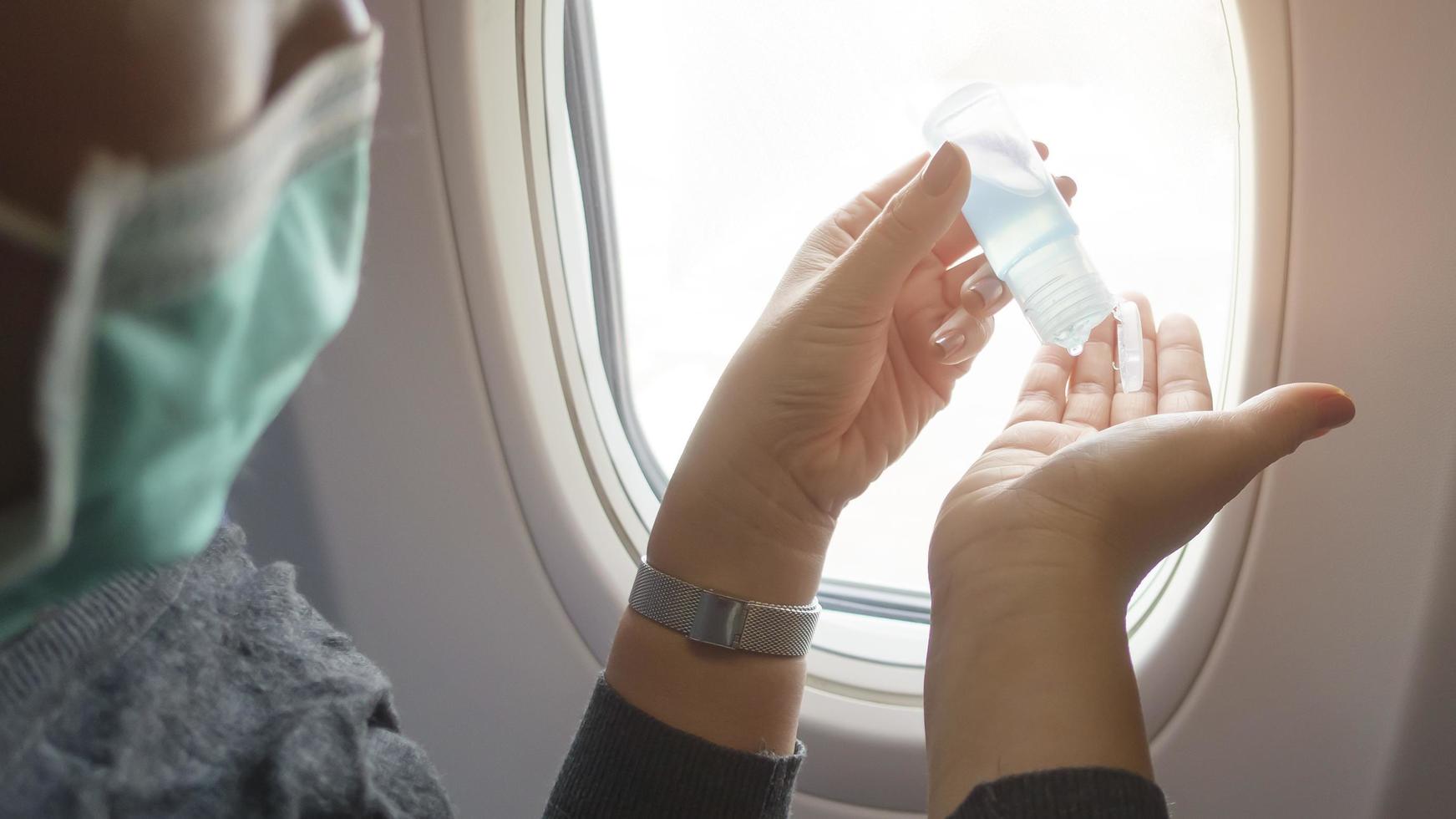 Close up hand of woman with protective mask is using alcohol gel onboard, covid-19 protection, new normal travel concept photo