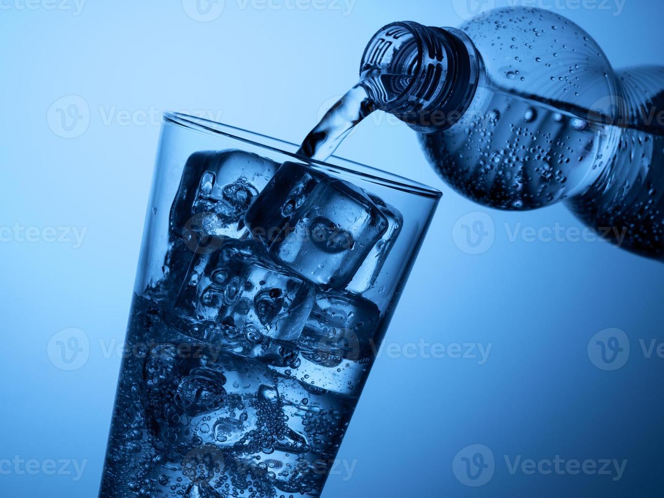 pouring  water from a plastic bottle into a glass with ice on a light blue background photo