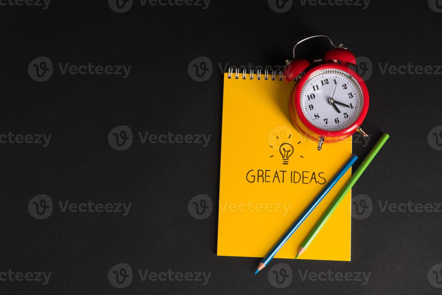alarm clock with notepad and colored pencils on black background, isolated. back to school. great ideas photo
