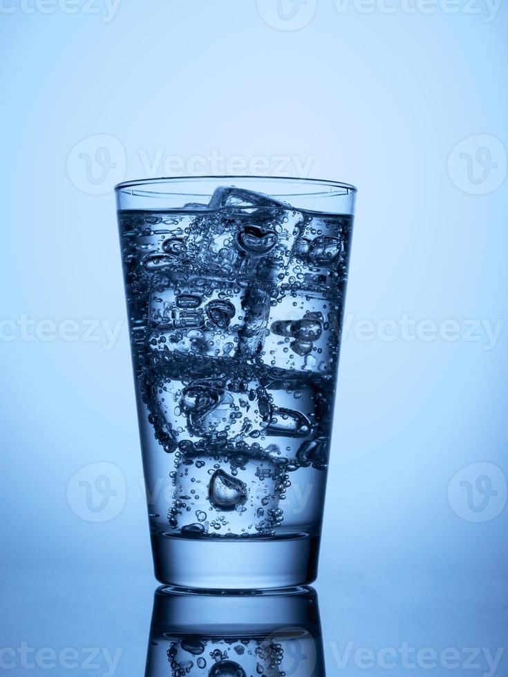 glass of water with ice cubes on a light blue background with reflection photo