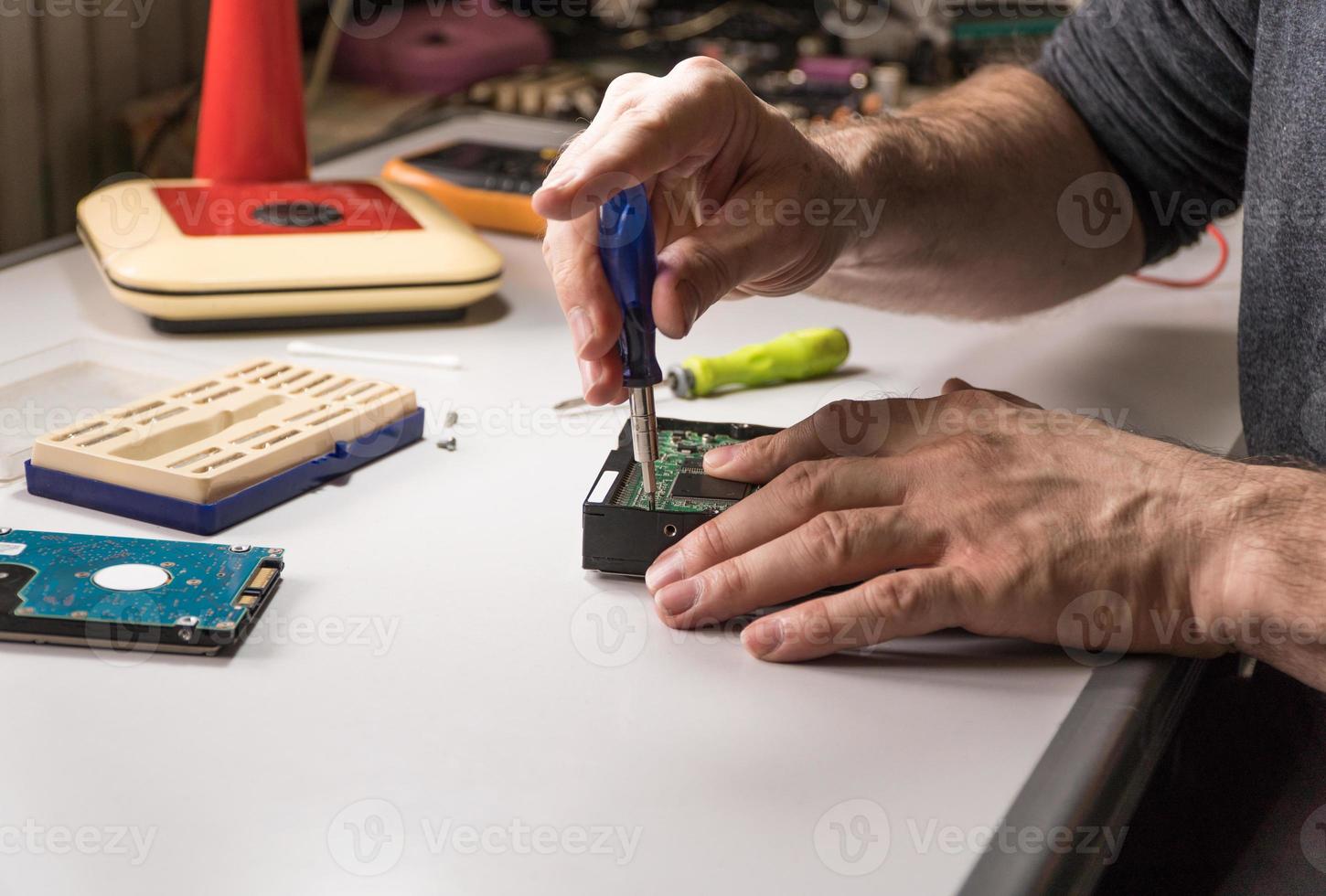 electronic engineer repairs computer hard drive. technologist with a screwdriver disassembles hdd photo