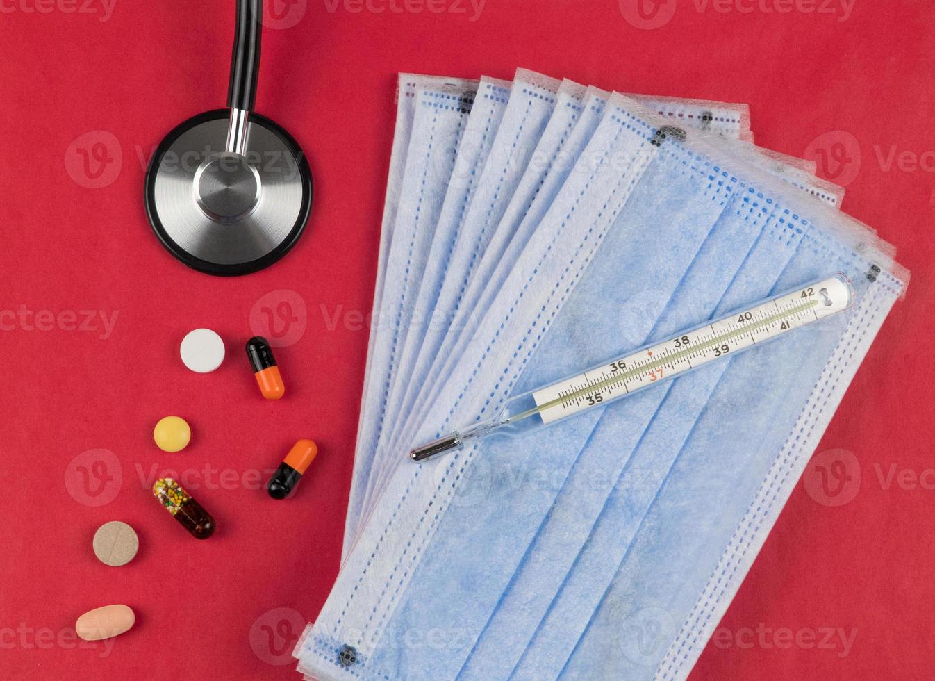 Medical protective masks on a red background with tablets, a thermometer and a stethoscope.. Coronavirus Protection Concept photo