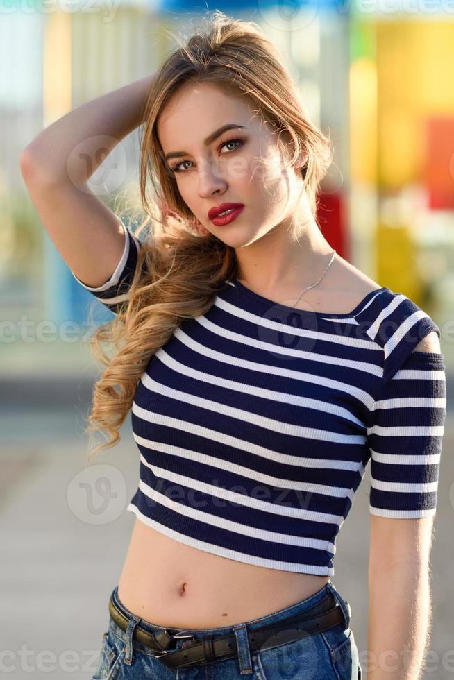 Blonde woman, model of fashion, sitting in urban background. photo