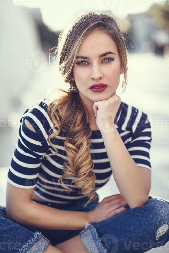 Blonde woman, model of fashion, sitting in urban background. photo