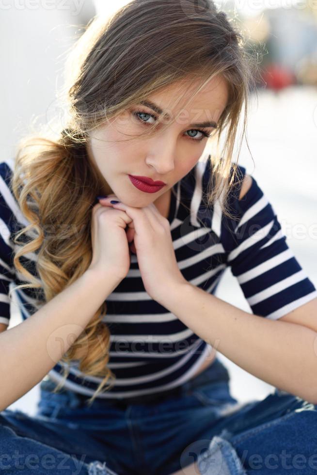 Blonde woman, model of fashion, sitting in urban background. photo