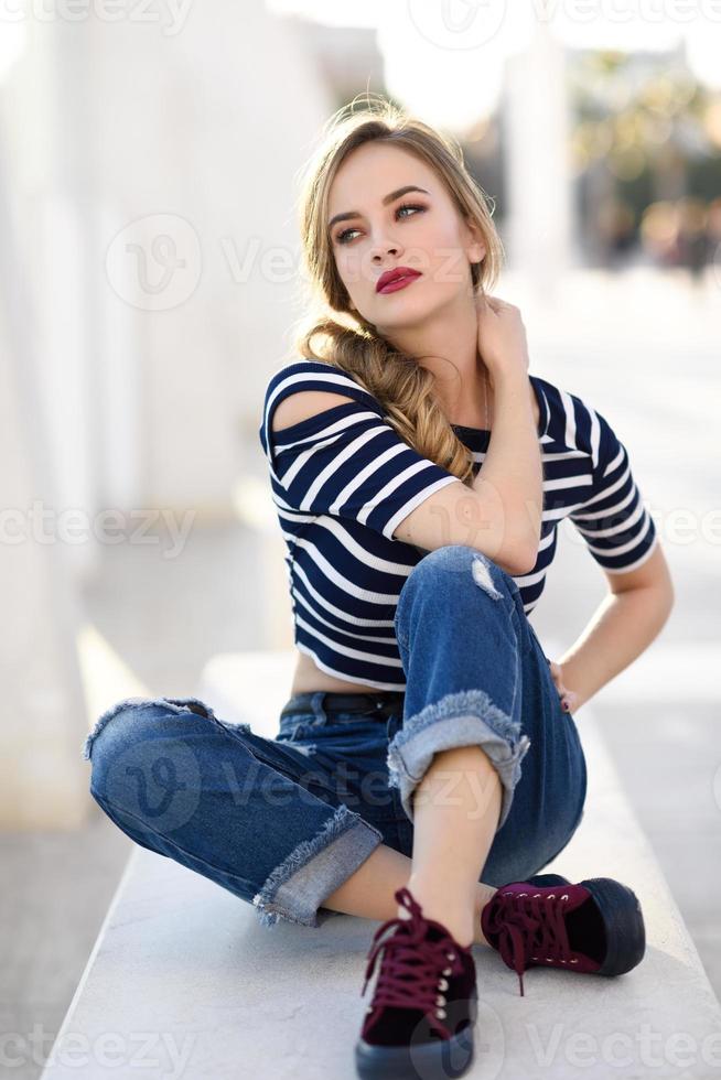 Blonde woman, model of fashion, sitting in urban background. photo