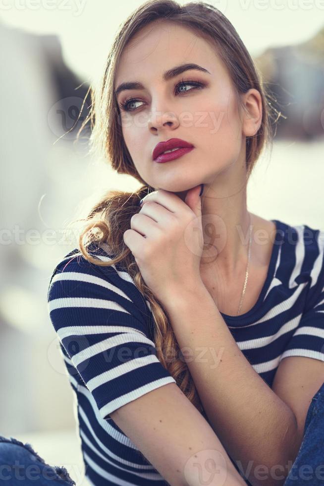 Blonde woman, model of fashion, sitting in urban background. photo